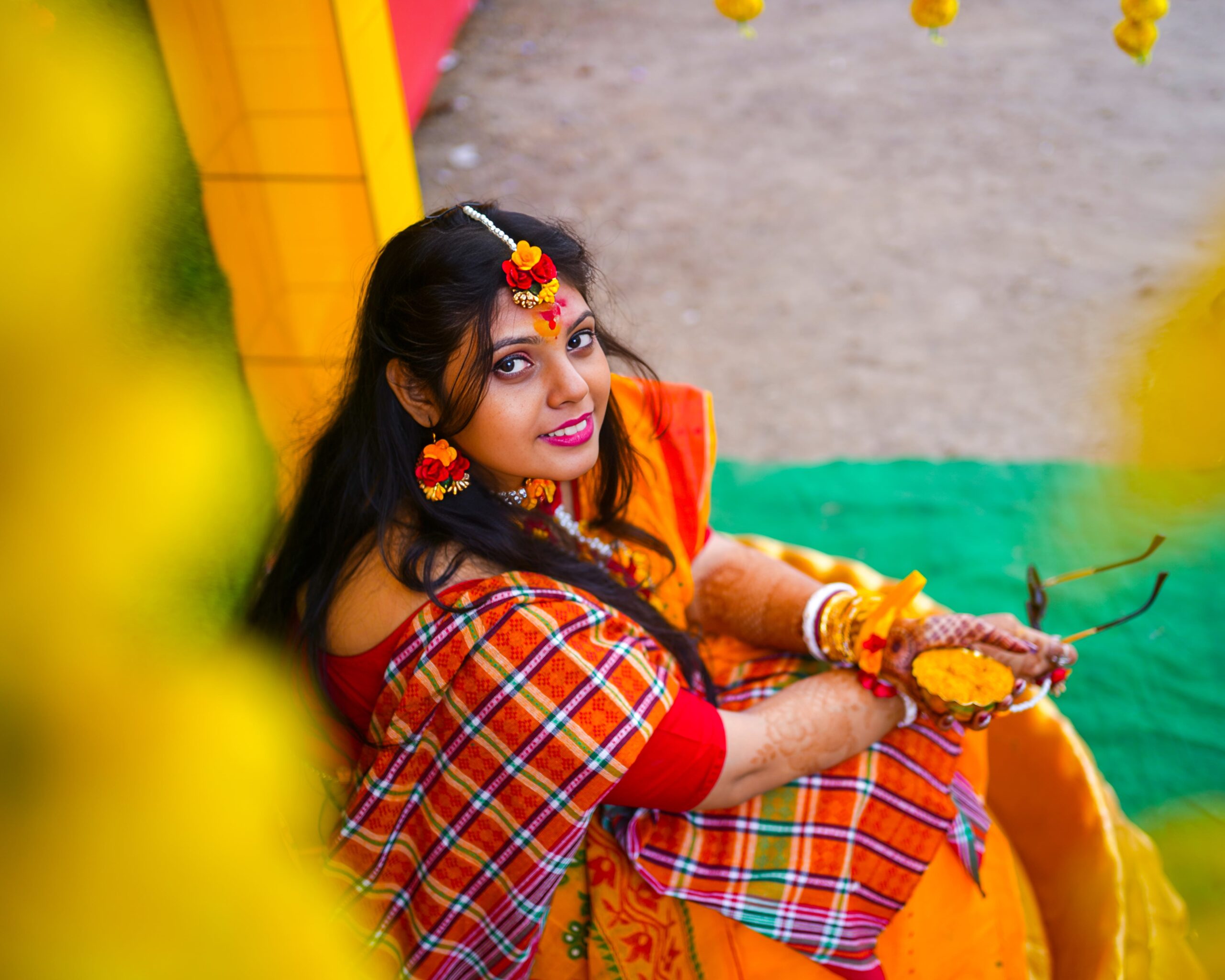 A woman wearing a traditional Indian sari sits gracefully on a yellow chair, showcasing vibrant colors and cultural elegance.