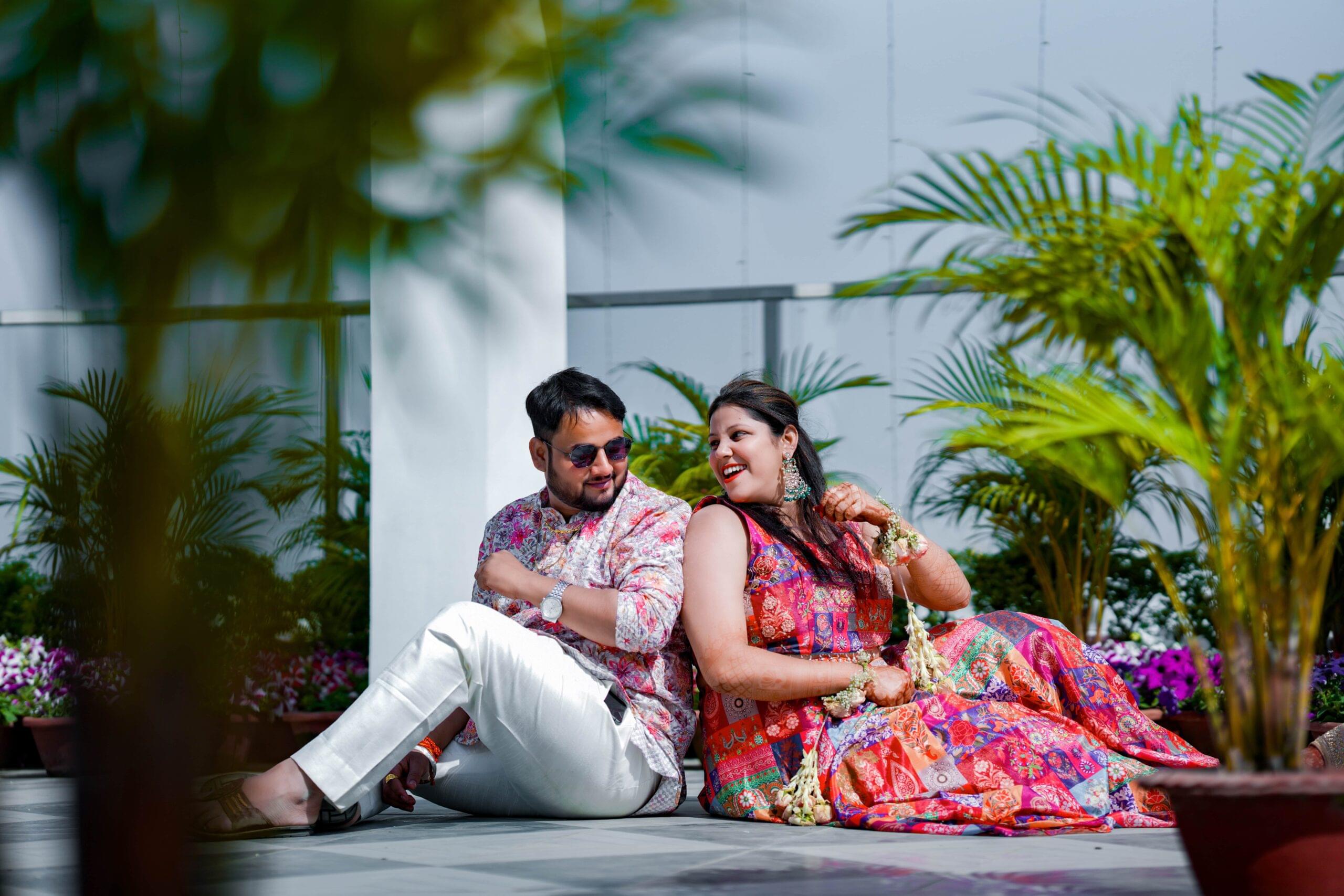 Couple in colorful outfits smiling outdoors, surrounded by potted plants.